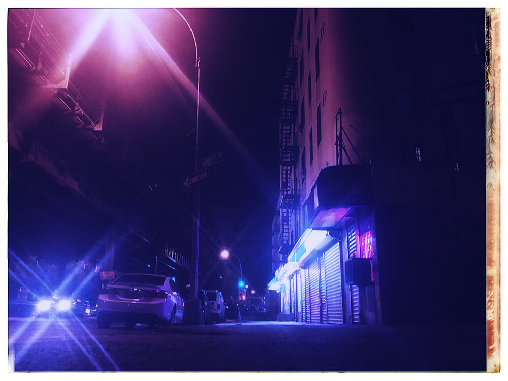 an edited photo titled 'Ambiguous Time', from the City Slick collection of JTJ' White's City Series photography. This is a photograph of a bodega along Morris Avenue in The Bronx at night with a dark blue hue.